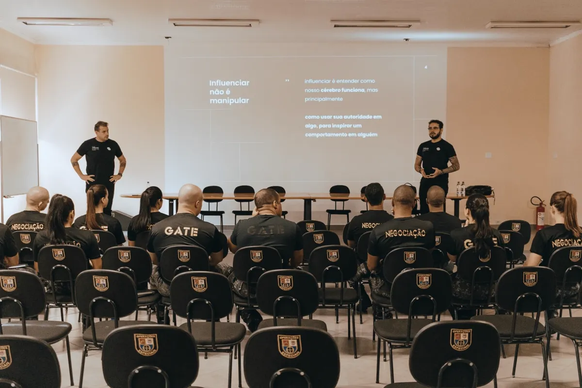 Turma acompanhando uma sessão em auditório, com dois facilitadores conduzindo a apresentação.