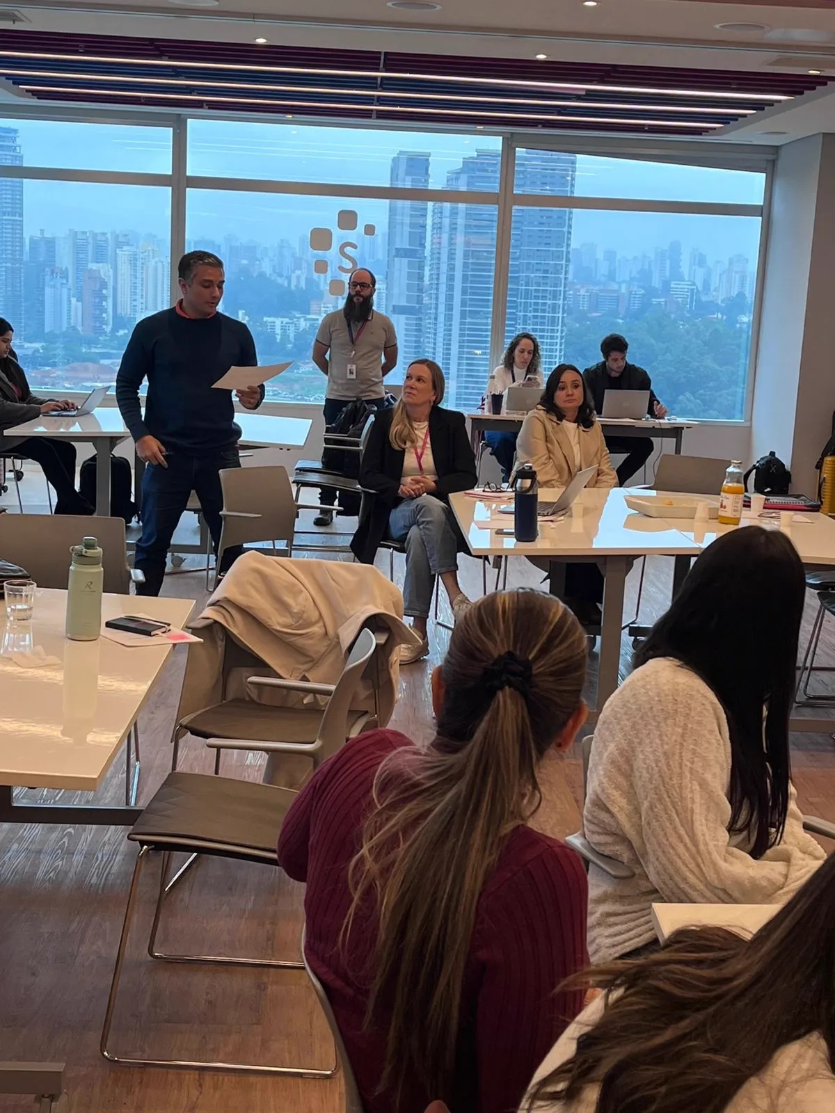 Sessão de trabalho com participantes em mesas e facilitador conduzindo a discussão.