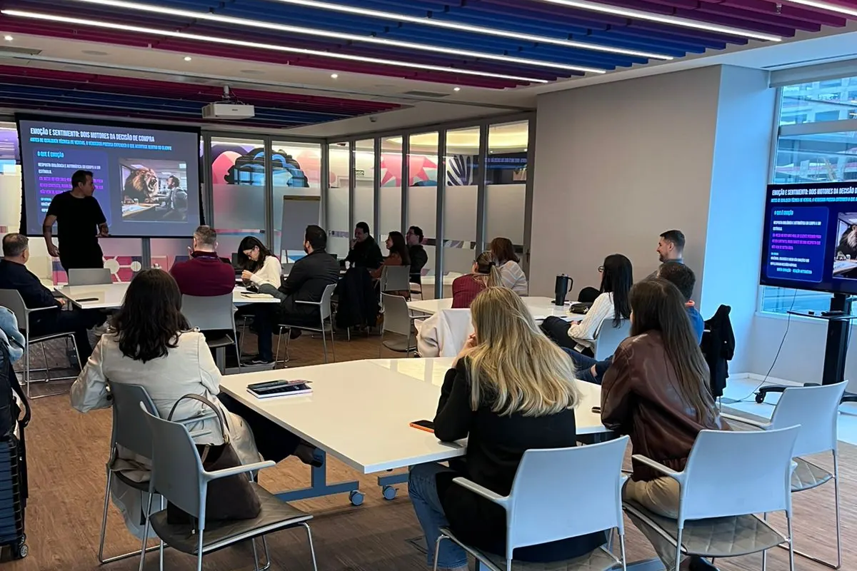 Sala corporativa preparada para um workshop, com o grupo em mesas de trabalho voltadas para a apresentação.